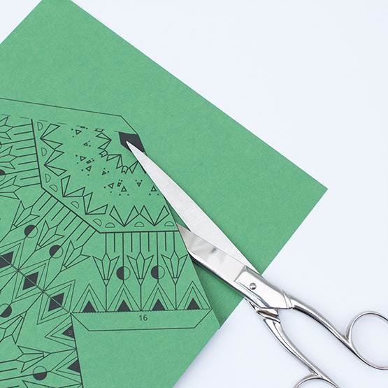 Close-up of scissors cutting out a green craft template with a black geometric pattern for an XXL Christmas star.