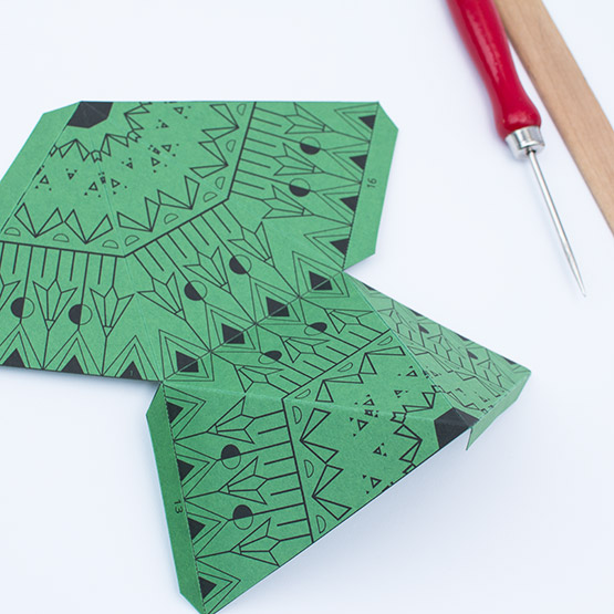 Using a ruler and an awl to score dashed lines on a green paper template for an XXL Christmas star.