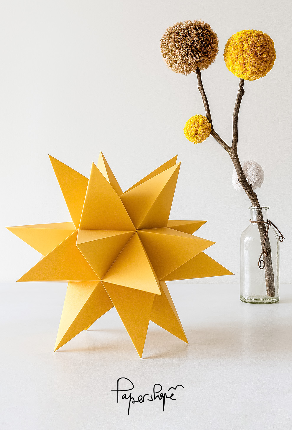 XXL paper Christmas star craft - large 3D star decoration in gold with twig and colorful pompoms in glass vase, minimalist Christmas decoration.