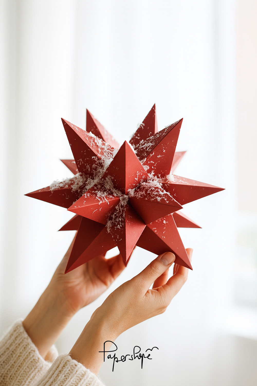 XXL Weihnachtsstern basteln: Roter geometrischer Papierstern mit Schneeflocken, gehalten von weiblichen Händen im Tageslicht.