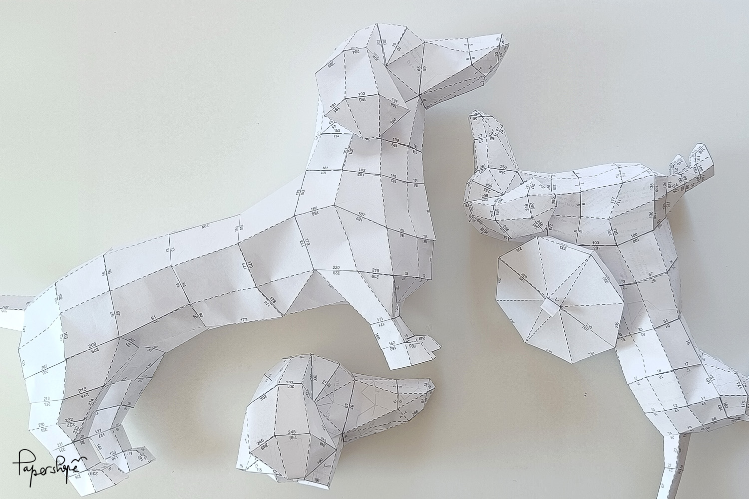 Mehrere gebastelte 3D Papier-Dackel aus Kopierpapier - DIY Bastelvorlagen mit nummerierten Laschen, Prototypen von Papershape auf hellem Untergrund.