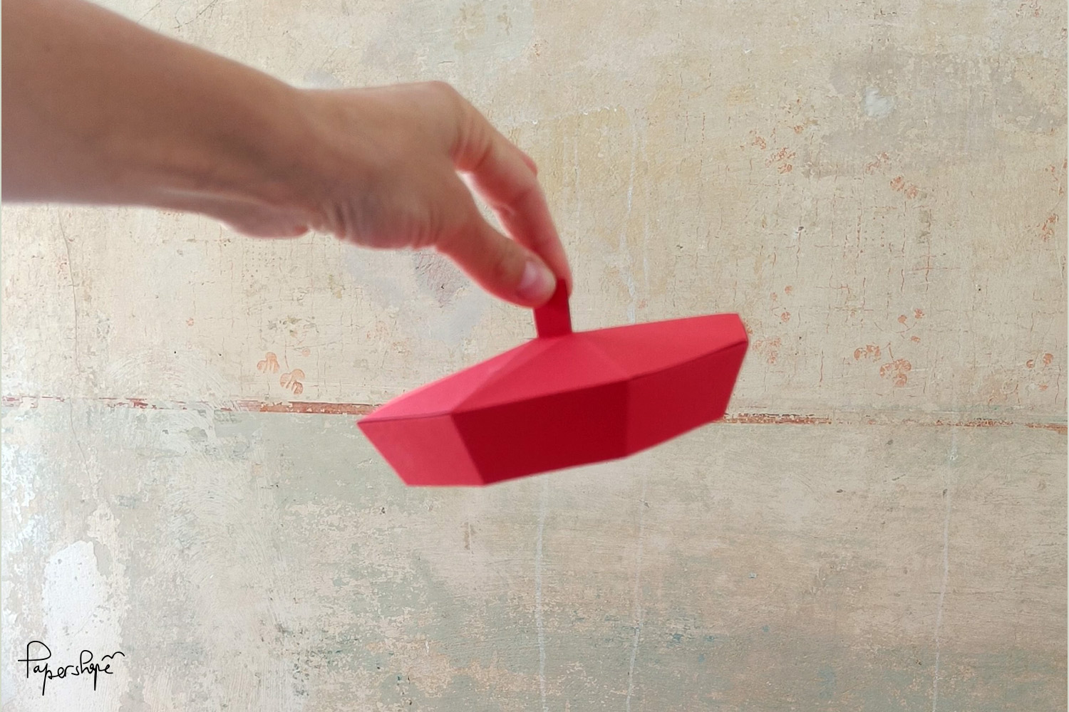 Rote Baskenmütze aus Papier im low poly Stil, gehalten von einer Hand