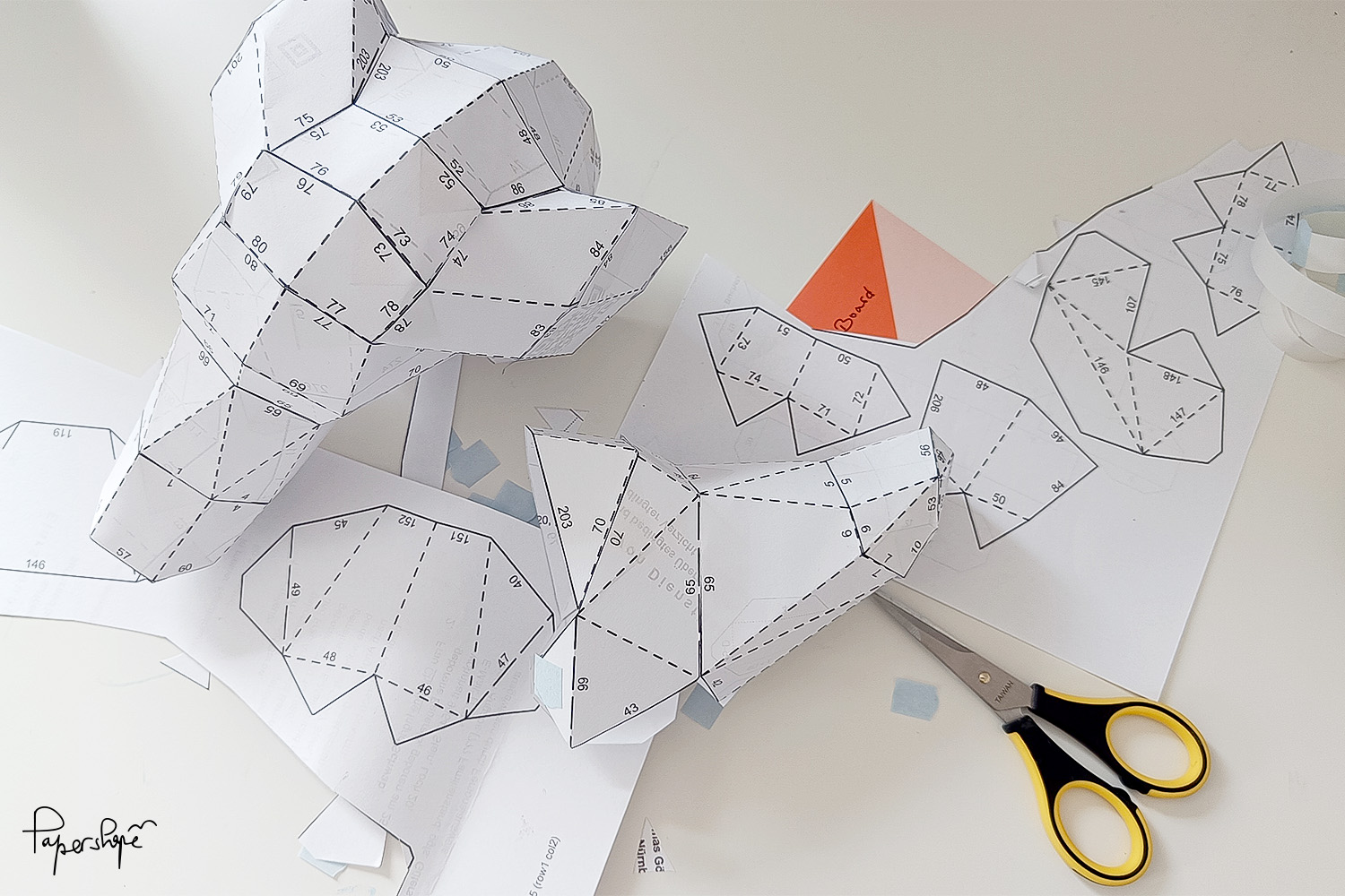 Papierbastelset für 3D Dackel von Papershape: ausgeschnittene Bastelvorlage aus Kopierpapier, Prototyp mit sichtbaren Klebelaschen und Zahlen, Bastelschere auf hellem Arbeitstisch