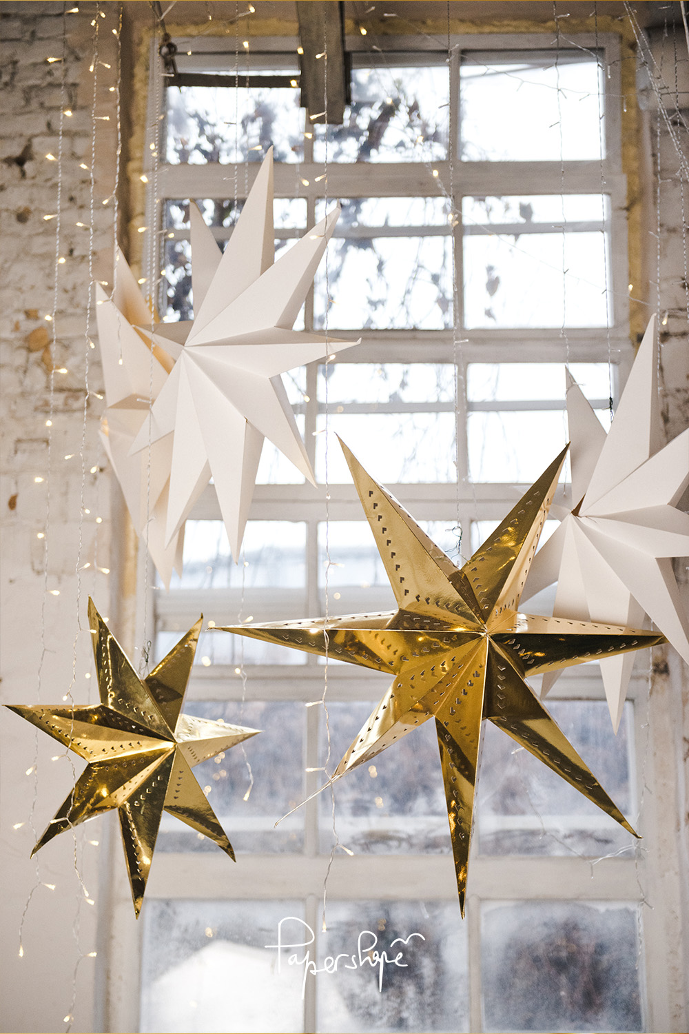 Hanging 3D paper stars in white and gold in front of a window - stylish do-it-yourself Christmas decorations
