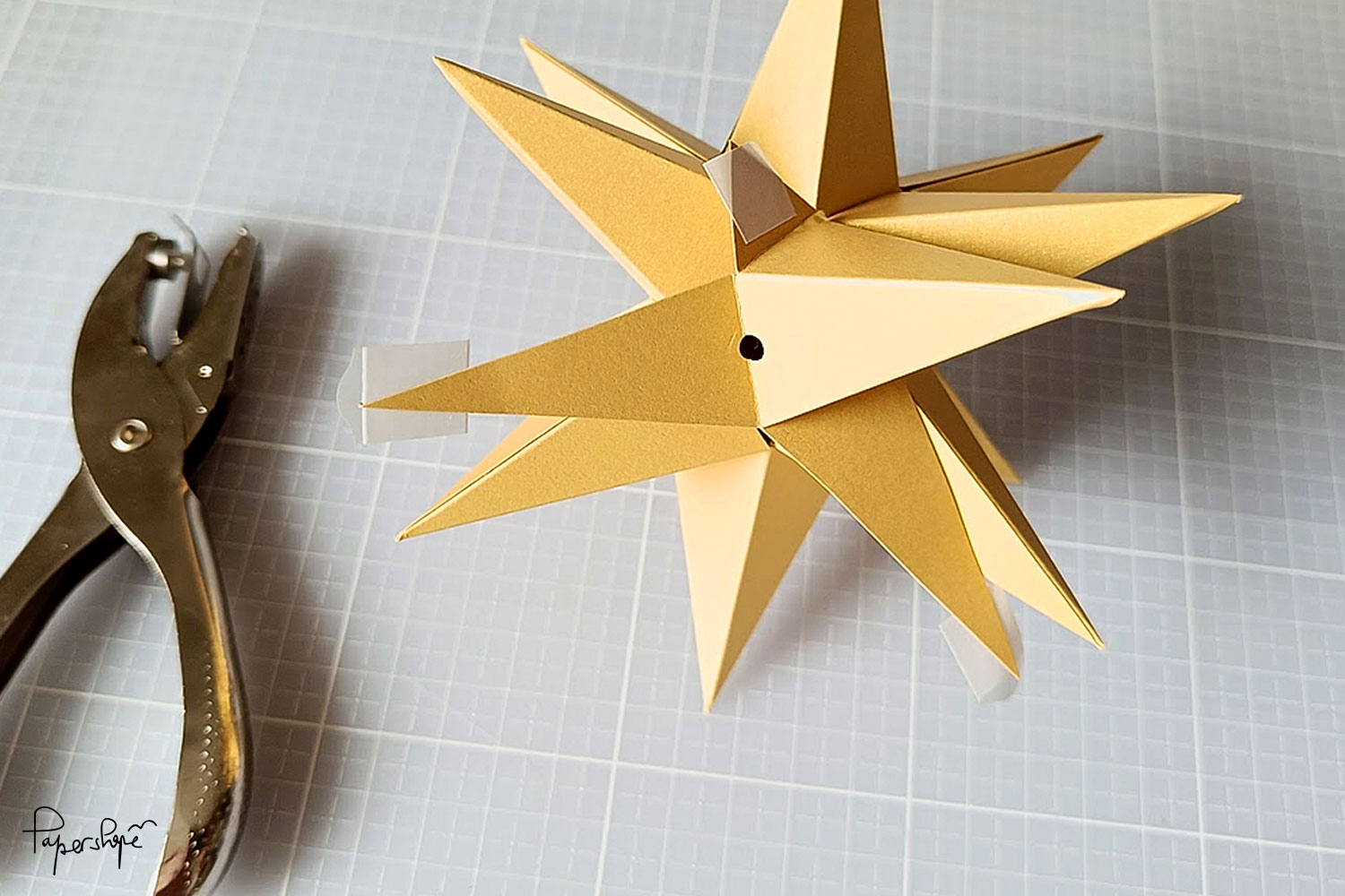Finished half of the 3D paper Christmas star with hole for hanging - hole punch pliers next to it