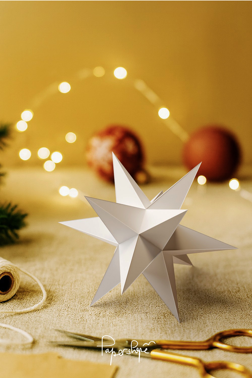 White Christmas star made of paper with 12 points as table decoration, atmospherically arranged in front of golden fairy lights and Christmas tree baubles