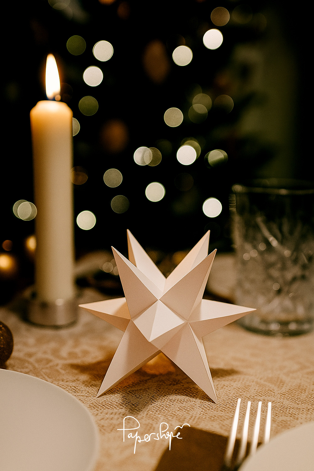 White Christmas star with 12 points made of paper as festive table decoration next to candle and cutlery