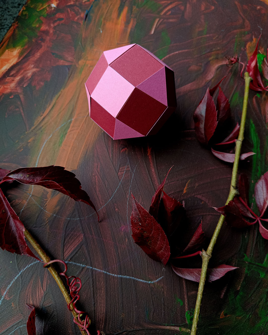 Red geometric paper pendant nestled among autumn leaves - atmospheric paper decor.