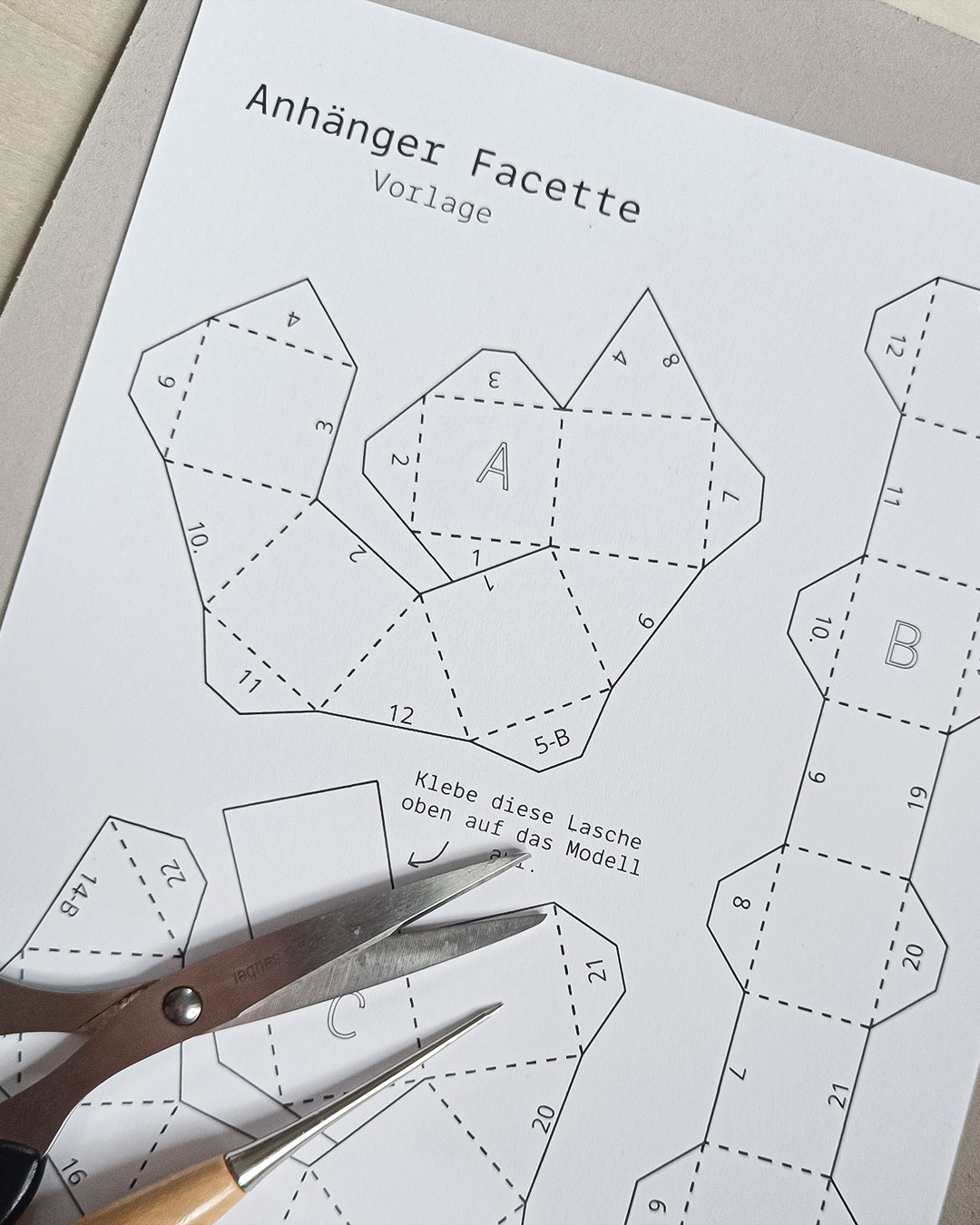 Printed template for a paper pendant with scissors and an awl.