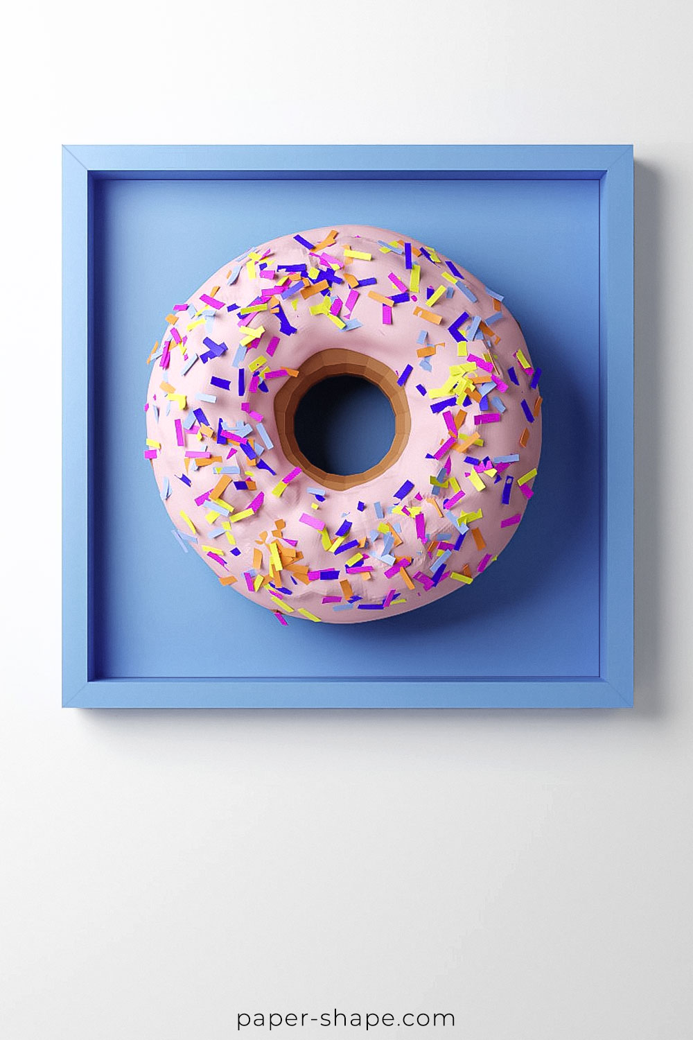 DIY Papier-Donut mit pinker Glasur und bunten Streuseln in einem blauen IKEA-Bilderrahmen als Wanddeko.