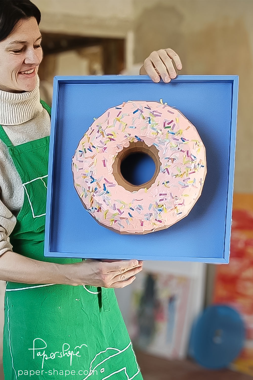 Anastasia von PaperShape hält fertigen Papier-Donut im blauen Rahmen – DIY-Projekt wird in Video erklärt.